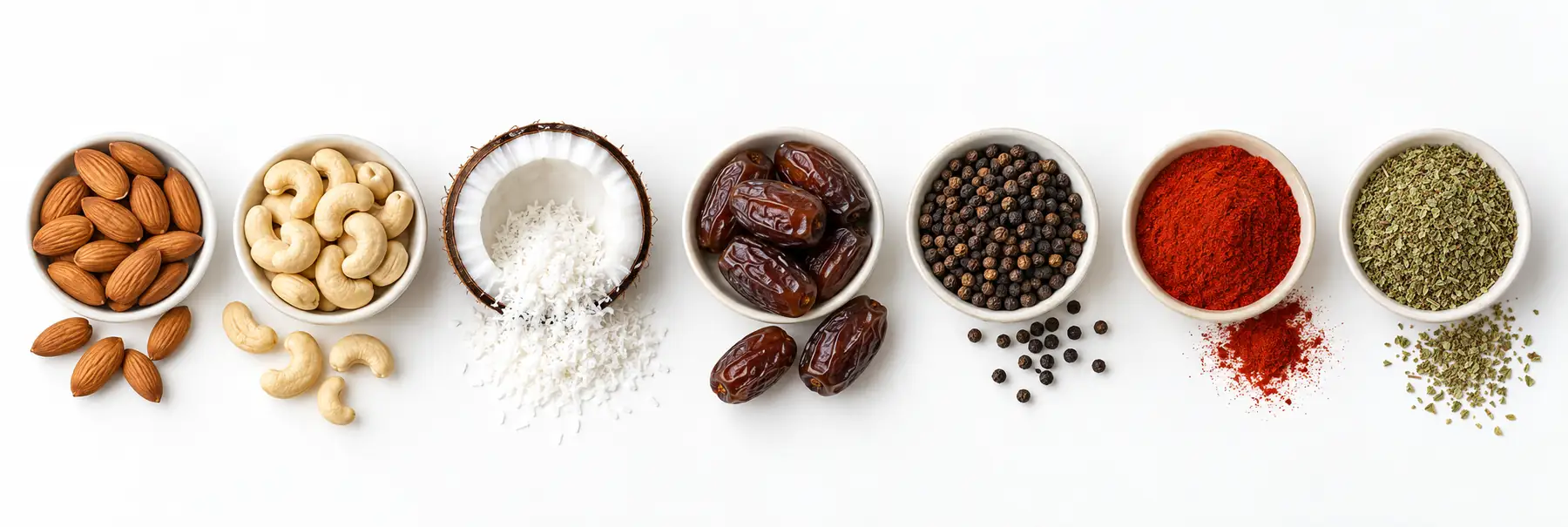 Seven of our products seen from above: almonds, cashew nuts, coconut, dates, black pepper, paprika and oregano